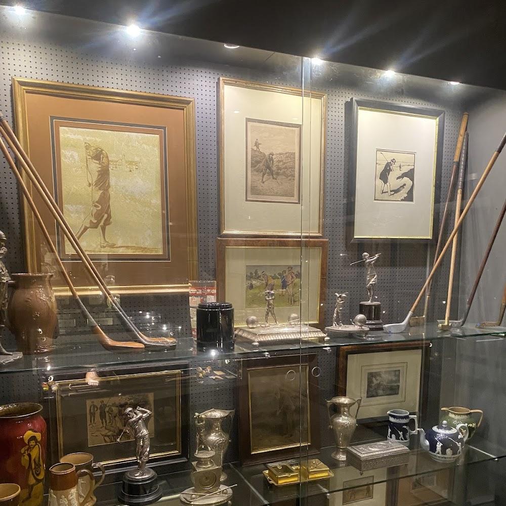 Framed golf-themed artwork and sculptures in a glass display cabinet.